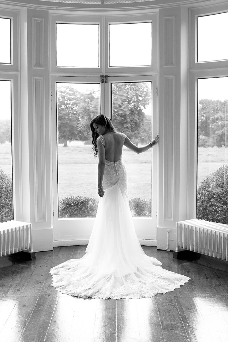 Shot of bride in wedding dress standing at window looking back